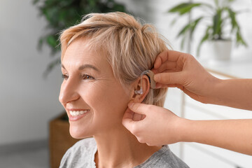 Young woman putting hearing aid in mature woman's ear in room