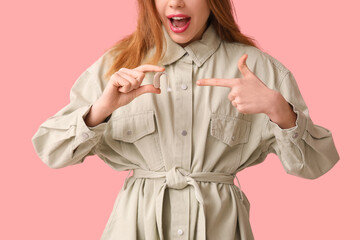 Young woman pointing at hearing aid on pink background