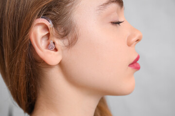Fototapeta premium Beautiful young woman with hearing aid on grey background, closeup