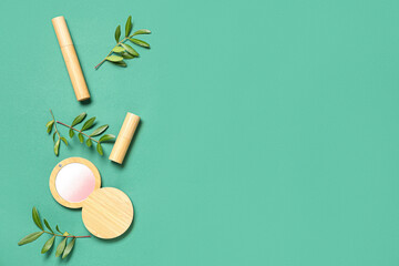 Highlighter, lipstick, mascara and leaves on green background
