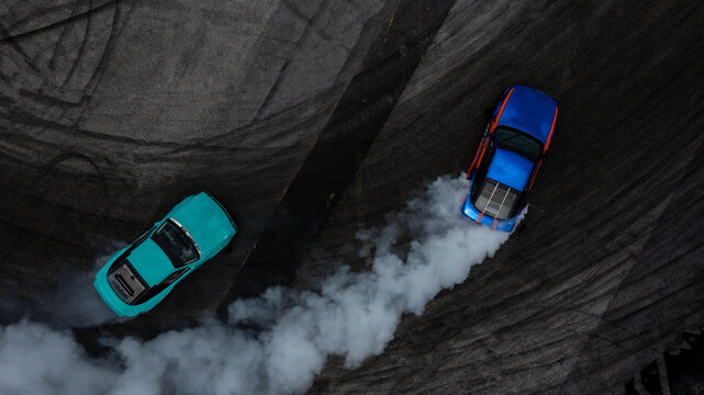 Aerial top view two cars drifting battle on asphalt race track with lots of smoke from burning tires, Two race cars competition drift battle view from above.