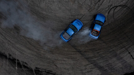 Aerial top view two cars drifting battle on asphalt race track with lots of smoke from burning...