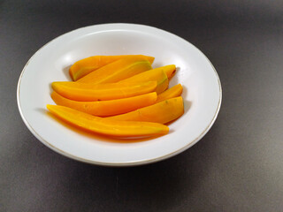 Long sliced orange carrots neatly placed in a white bowl, set against a dark grey ash background, offering a vibrant pop of color and a striking visual contrast