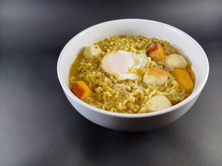Indomie Rebus with Sausages, Meatballs, and Sunny Side Up Egg: Flavorful Indonesian Noodle Dish Served in a White Bowl, Perfectly Complemented by a Dark and Ash Abstract Background
