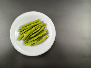Chopped green beans neatly placed in a white bowl, set against a contrasting dark grey ash background, creating a visually striking and appetizing presentation