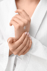 Woman in bathrobe applying cream on her hands, closeup
