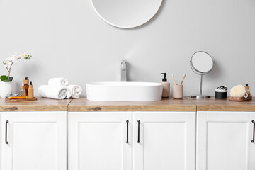 Sink and bath supplies on chest of drawers near light wall in bathroom