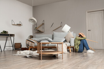 Young woman sitting near sofa during earthquake at home