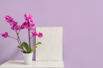 Orchid flower with painting on commode near lilac wall