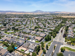 Drone photo over a suburban neighborhood in Brentwood, California with homes, streets and a blue sky