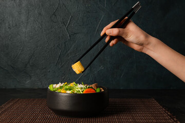 Woman eating tasty rice with chicken and vegetables on dark background, closeup
