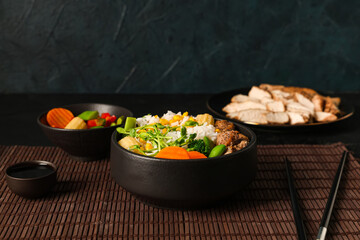 Bowls of tasty rice, chicken, vegetables and soy sauce on dark background