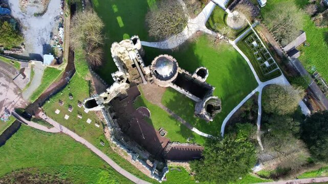Top-down aerial orbit view of Laugharne Castle, medieval stone structure and surrounding meadow, Wales