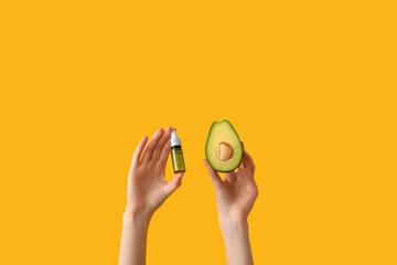 Female hands with bottle of cosmetic product and avocado on pink background