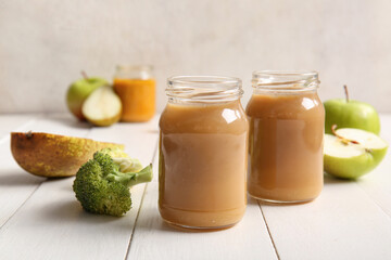 Glass jars of healthy baby puree and ingredients on light wooden table