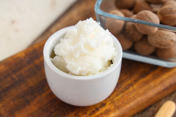 Wooden board with bowl of shea butter and nuts, closeup