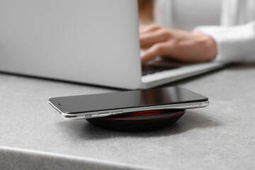 Mobile phone charging with wireless pad and working woman on background