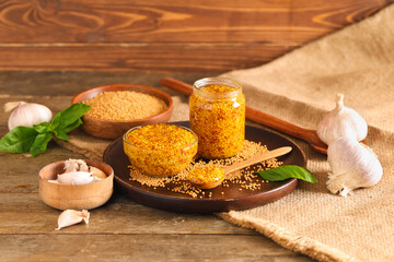 Jar and glass bowl of Dijon mustard with basil on wooden background