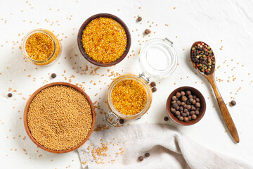 Jars and bowls of Dijon mustard with seeds and peppercorn on white background