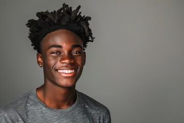 Fototapeta premium A close-up photograph of a young Black student standing with a bright smile, looking directly at the camera against a gray backdrop