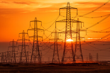 Sun setting behind the electric power lines running from Dungeness power station on the Kent coast south east England UK