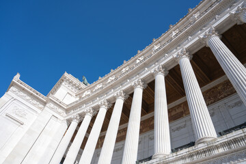 A low-angle view of the white marble columns of the Vittoriano monument in Rome, Italy, against a clear blue sky.