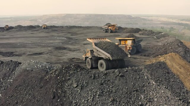 Large quarry dump truck. Loading rock in dumper. Loading coal into truck. Mining car machinery to transport coal. Open pit mine quarrying extractive industry stripping work. Big Yellow Mining Trucks