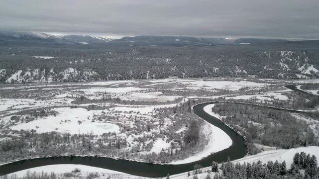 Dark serpentine river in white winter snow, monochrome aerial view