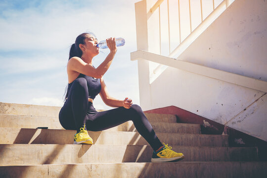 Tired runner woman with a bottle of electrolyte drink freshness after training outdoor workout at the stadium stairway.