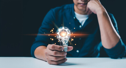 A male hand holds an illuminated light bulb, symbolizing new ideas, innovative technology, and...