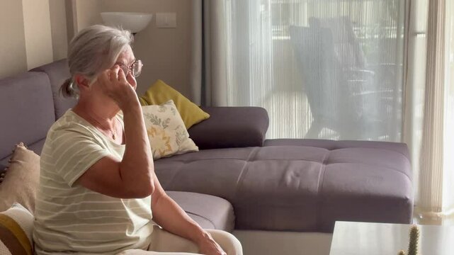 Side view scene of mature lady wearing eyeglasses at home sitting on sofa. Eyesight and age problems mature female people in indoor leisure activity alone relaxing on couch
