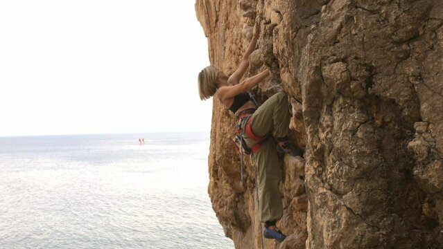 A woman is climbing a rock wall with a view of the ocean in the background