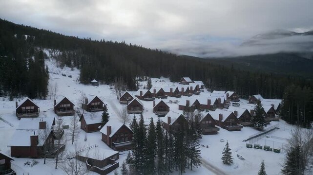 Aerial ascends from monochrome winter mtn resort under heavy overcast