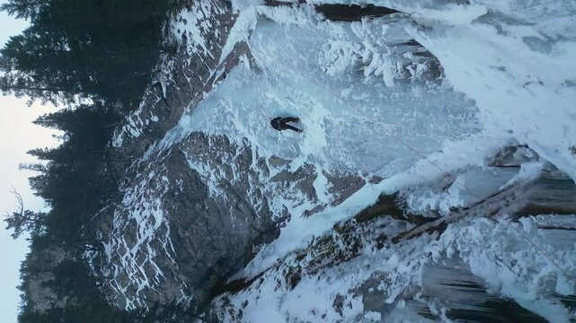 Vertical format Ice climber climbs steep frozen waterfall on mtn cliff