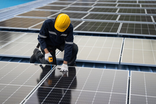 Engineer worker using electric drill repairing on solar cell panel on the roof of the factory. After service and security for industrial renewable energy concept