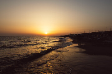 Sunset on the Mediterranean Sea. Natural seascape with calm waves and bright low sun. Side view of the water and beach. The concept of an evening walk. Coastline. Holidays in Italy. Nature wallpaper