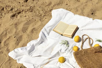Fresh lemons, book, wicker bag  and olive twigs on the white sheet on the beach. Summer vacation background, copy space for your text. © Nika Votinova