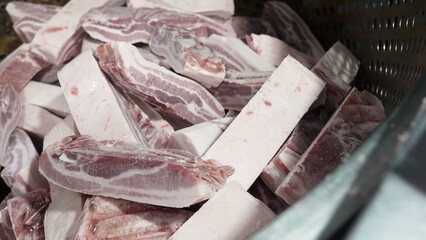 A professional butcher in white gloves is meticulously cutting large pork ribs into smaller portions using a mechanical saw.