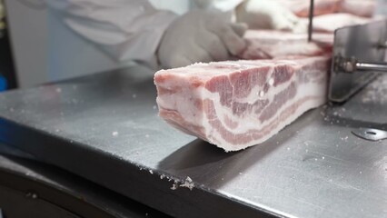 A professional butcher in white gloves is meticulously cutting large pork ribs into smaller portions using a mechanical saw.