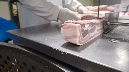 A professional butcher in white gloves is meticulously cutting large pork ribs into smaller portions using a mechanical saw.