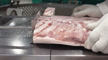 A professional butcher in white gloves is meticulously cutting large pork ribs into smaller portions using a mechanical saw.