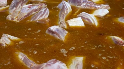 Pork ribs are being cooked on an industrial scale in large pans, simmering in a rich broth.
