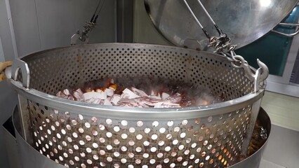 Pork ribs are being cooked on an industrial scale in large pans, simmering in a rich broth.