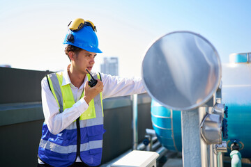 Technician talking on walkie talkie and checking pipeline valves or water tank area at urban...