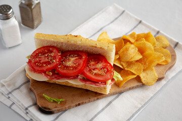 Homemade Italian Sub Sandwich with Salami, Tomatoes and Shredded Iceberg Lettuce on a rustic wooden board, side view.