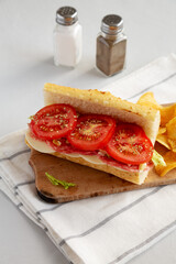 Homemade Italian Sub Sandwich with Salami, Tomatoes and Shredded Iceberg Lettuce on a rustic wooden board, side view.