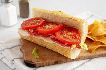 Homemade Italian Sub Sandwich with Salami, Tomatoes and Shredded Iceberg Lettuce on a rustic wooden board, side view.