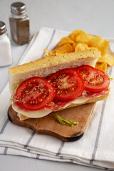 Homemade Italian Sub Sandwich with Salami, Tomatoes and Shredded Iceberg Lettuce on a rustic wooden board, side view.