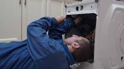 a man repairs a washing machine lying, plumber lies in the kitchen and repairs an old broken washing machine, home appliance repair specialist