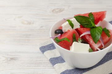 Summer salad with watermelon, feta cheese, olives and mint in a white bowl on a white wooden table. Concept of healthy eating. Vegan, vegetarian. Horizontal orientation. Selective focus. Copy space